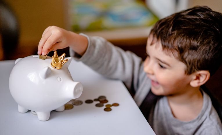 A child putting a coin into a piggy bank, relevant to compulsory financial education in schools